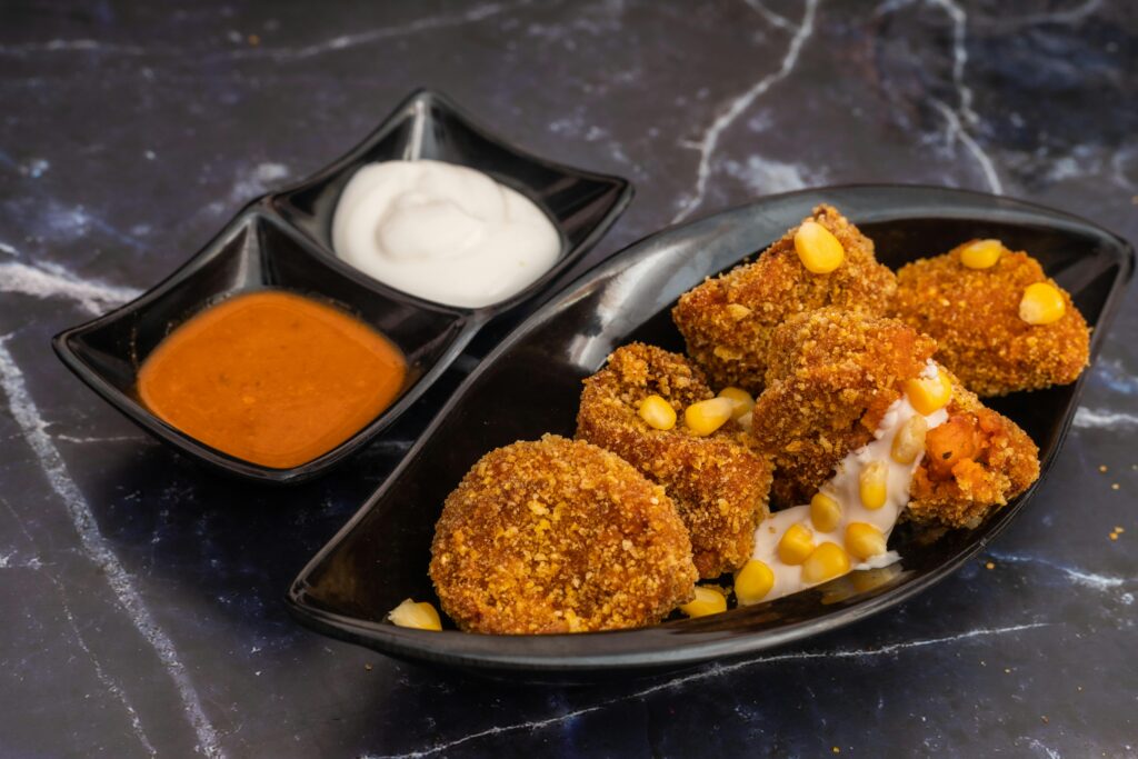 Delicious crispy cheese corn momos served with spicy and creamy sauces on a marble surface.